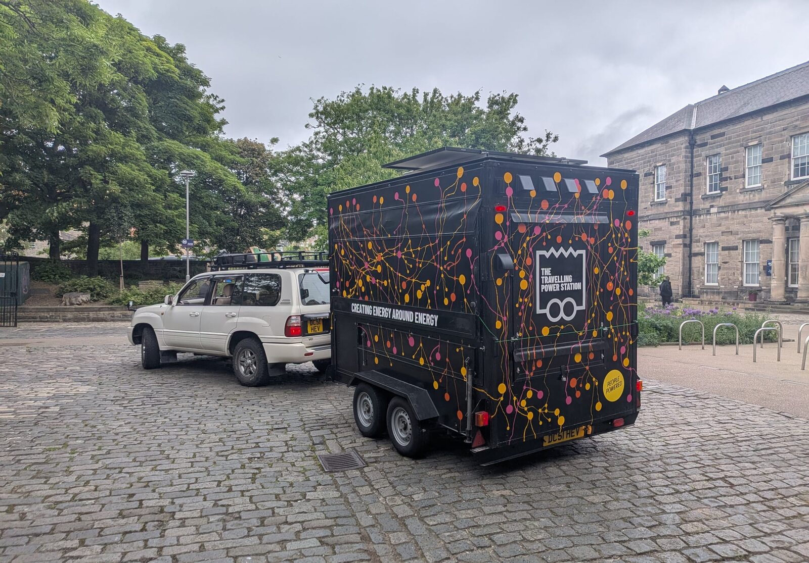 The Travelling Power Station trailer with black circuit artwork parked behind a white vehicle